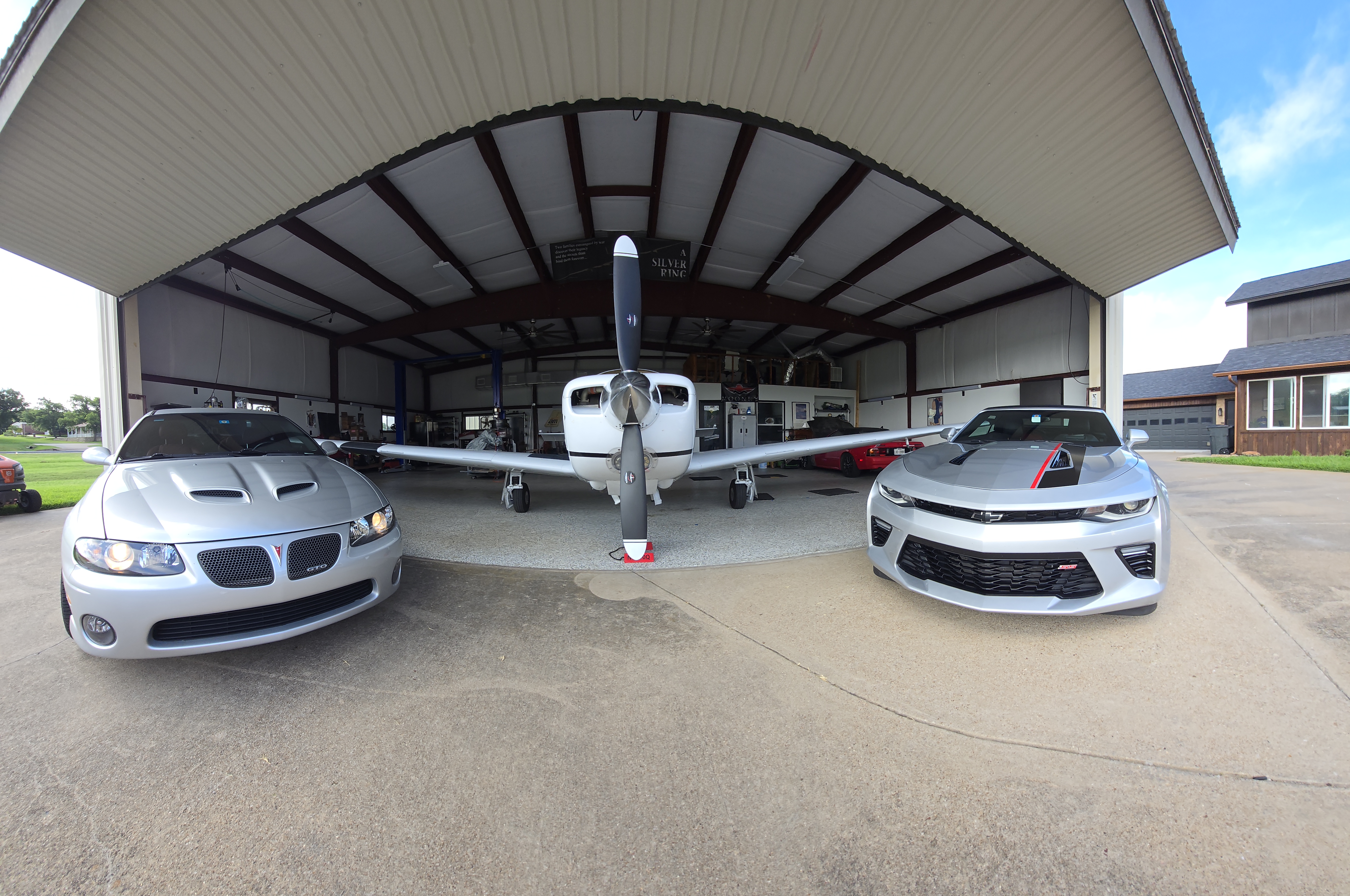 Hangar exterior with bi-fold door open, GTO and Camaro flanking Mooney