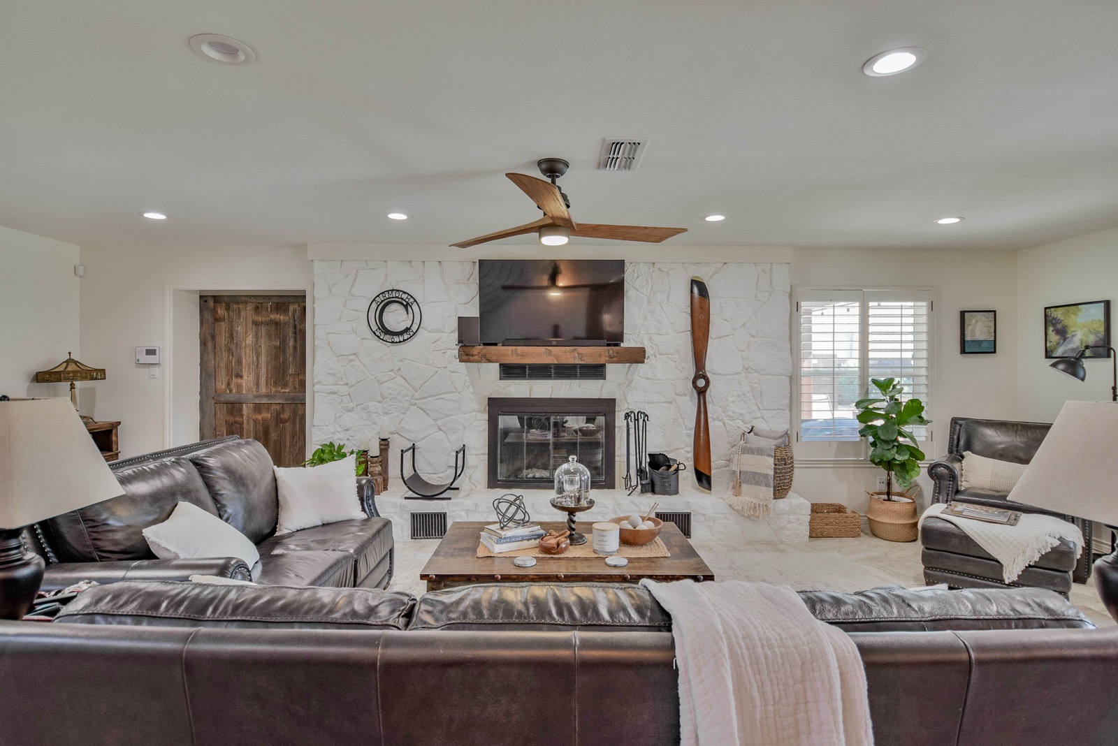 Living room with stone fireplace, leather sofas, and vintage propeller